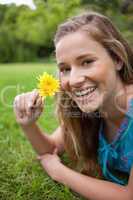 Smiling teenager holding a yellow flower while lying on the gras