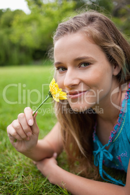 Young smiling girl lying in a park while smelling a flower and l