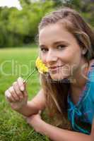 Young smiling girl lying in a park while smelling a flower and l