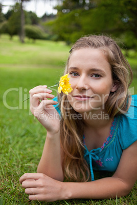 Young relaxed girl holding a yellow flower while lying in a park