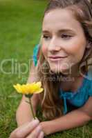 Young thoughtful girl lying on the grass while holding a flower