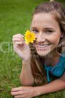 Smiling young woman showing a yellow flower while lying on the g