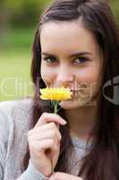 Young woman looking at the camera while smelling a yellow flower