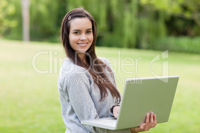 Young smiling girl standing upright in a public garden while usi