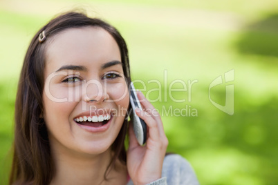 Young woman using her cellphone in a park while laughing