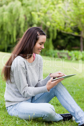 Smiling young girl using her tablet pc while sitting in a park