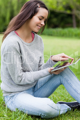Young smiling woman sitting on the grass in a park while using h