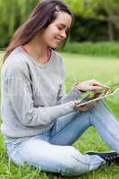 Young smiling woman sitting on the grass in a park while using h