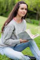 Thoughtful young woman holding a book while sitting on the grass