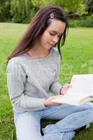 Young calm girl reading a book while sitting on the grass