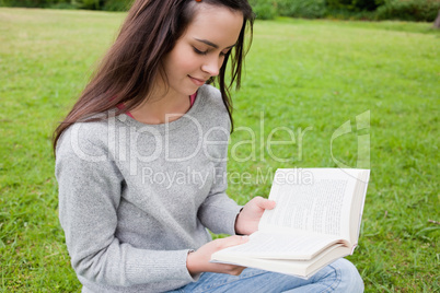 Young relaxed girl reading a book while sitting in a public gard