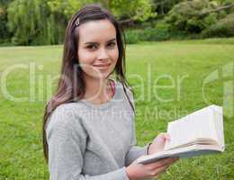 Smiling young girl standing upright in the countryside while rea