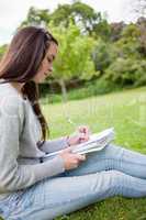 Side view of a young girl sitting on the grass while writing on