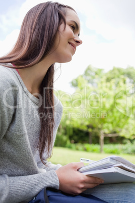 Smiling young student doing her homework while sitting on the gr