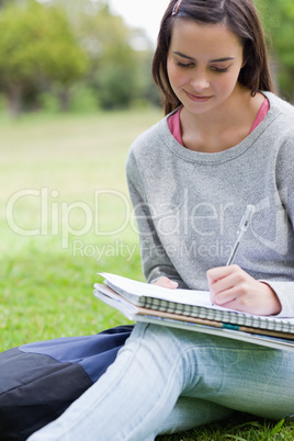 Young smiling girl writing on her notebook while sitting in a pa