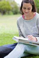 Young smiling girl writing on her notebook while sitting in a pa