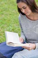 Serious young girl sitting on the grass while reading a book