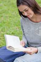 Young relaxed girl sitting in a public garden while reading a bo