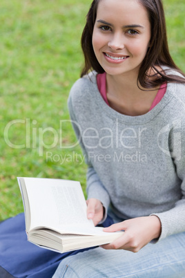 Young smiling woman reading a book in a park while looking at th