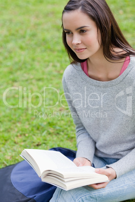 Young calm woman reading a book in a park while looking towards