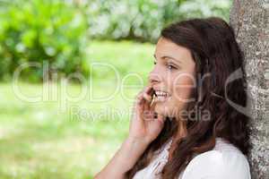 Young woman talking on the phone while leaning against a tree