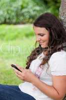 Young relaxed woman sending a text while sitting against a tree