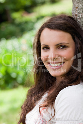 Young woman leaning against a tree while showing a beaming smile