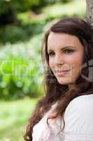 Young peaceful woman leaning against a tree while looking toward