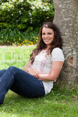 Young smiling woman sitting against a tree with arms crossed