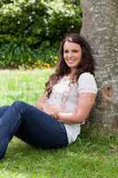 Young smiling woman sitting against a tree with arms crossed