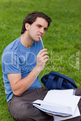 Young thoughtful man holding his pen while sitting on the grass