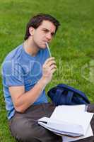 Young thoughtful man holding his pen while sitting on the grass