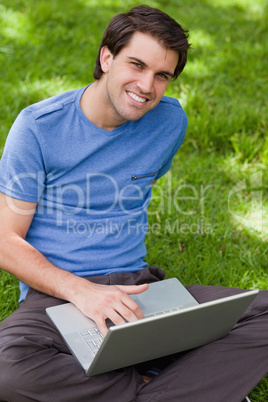 Young smiling man using his laptop while sitting cross-legged