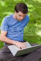 Young serious man working on his laptop while sitting in a park