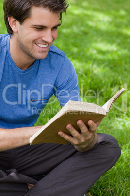 Young smiling man reading a book while siting on the grass