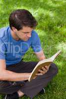 Young serious man sitting cross-legged while reading a book