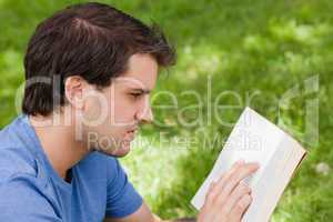 Young serious man reading a book while sitting in a park
