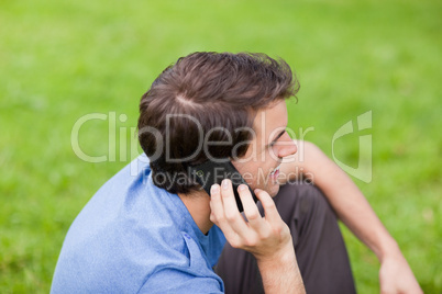 Young smiling man talking on the phone while sitting in a park