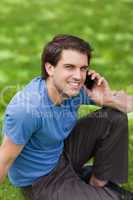 Young happy man using his mobile phone while sitting on the gras