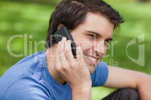 Smiling young man sitting in the countryside while using his cel