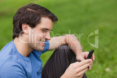 Young man sending a text with his cellphone while sitting on the