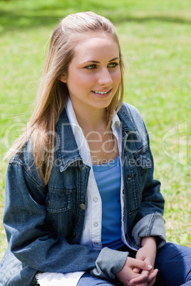 Young smiling girl sitting on the grass with hands crossed