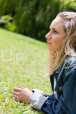 Young serious woman looking ahead while lying on the grass