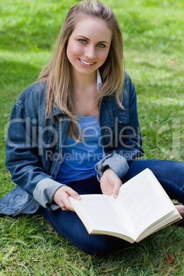 Young girl sitting cross-legged while holding a book and looking