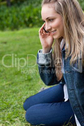 Young smiling girl talking on the phone while sitting on the gra