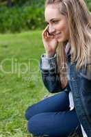Young smiling girl talking on the phone while sitting on the gra