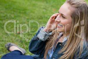 Young smiling blonde girl calling with her cellphone while sitti