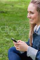 Young smiling woman sending a text while sitting in a park