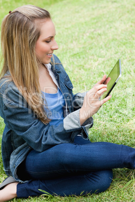 Young attractive blonde girl sitting on the grass while using he