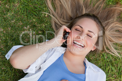 Young laughing girl lying on her back while talking on the phone